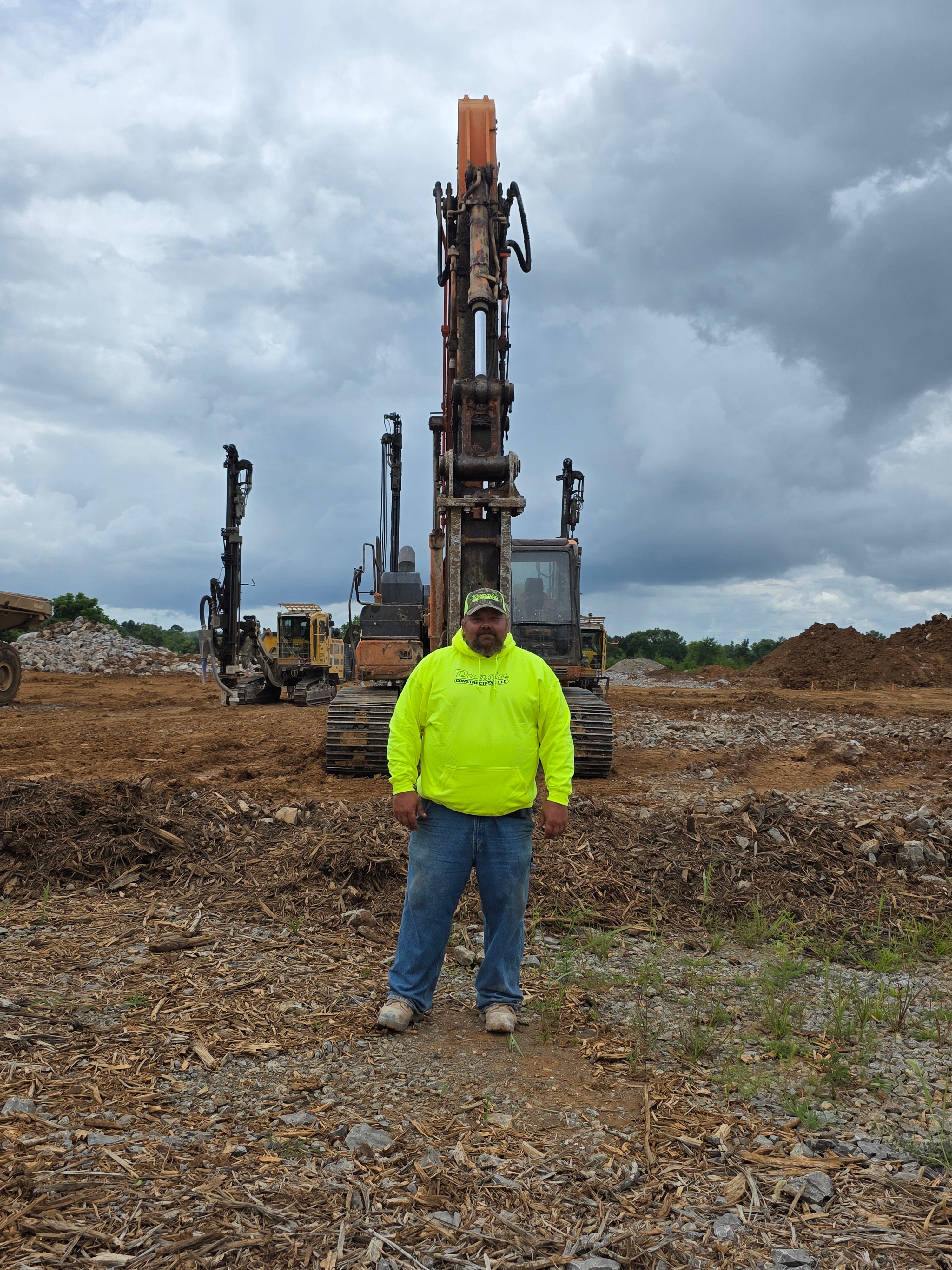 Person in a bright yellow safety jacket standing next to large drilling equipment on a construction site.